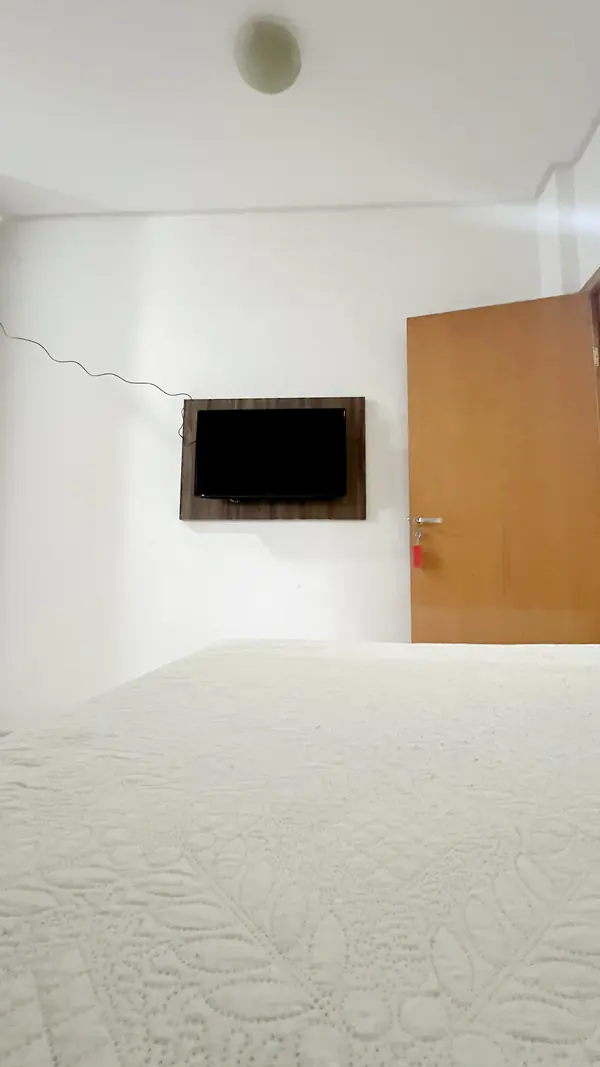 Cama de casal com TV na parede em frente